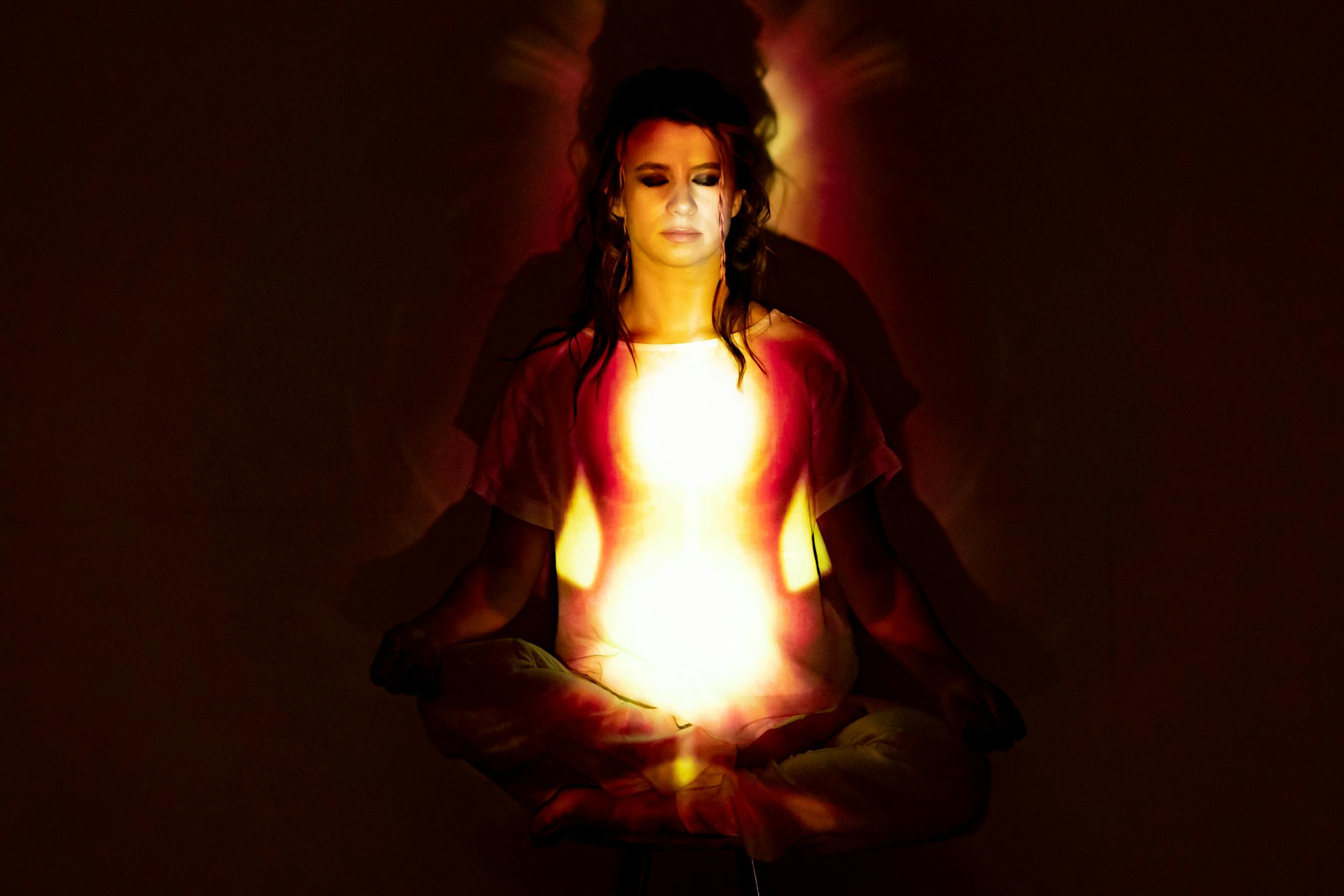 A woman in meditation surrounded by a radiant aura, symbolizing spiritual energy and enlightenment.